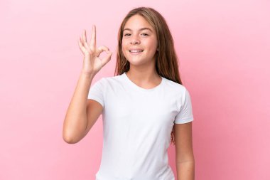 Pembe arka planda izole edilmiş küçük beyaz kız parmaklarıyla tamam işareti gösteriyor.