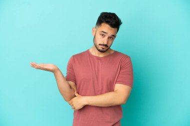 Kafkasyalı genç adam mavi arka planda izole edilmiş. Şüpheleri var.