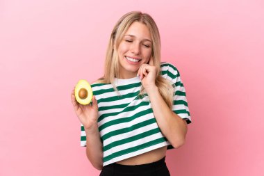 Pembe arka planda izole edilmiş avokado tutan beyaz bir kadın hayal kırıklığına uğramış ve kulaklarını kapatmış.