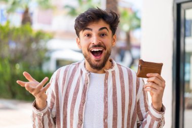 Yüzünde şok ifadesi olan yakışıklı bir Arap cüzdan taşıyor.