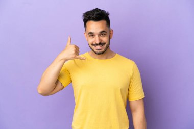 Mor arka planda izole edilmiş genç beyaz bir adam telefon jesti yapıyor. Bana geri dönüş işareti ver.