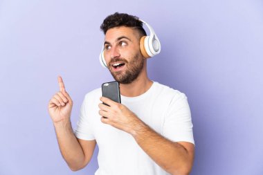 Mor arka planda izole edilmiş beyaz bir adam cep telefonuyla müzik dinliyor ve şarkı söylüyor.