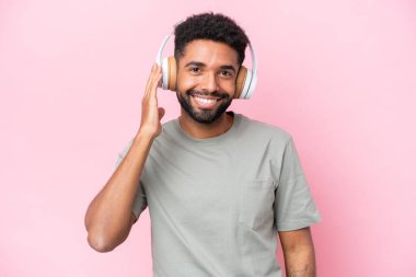 Pembe arka planda izole edilmiş genç Brezilyalı adam müzik dinliyor.