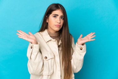 Mavi arka planda izole edilmiş genç beyaz kadın şüpheli hareketler yapıyor.