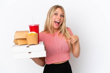 Mavi arka planda yağlı yiyecekler tutan beyaz kadın şaşırmış ve ön tarafı işaret ediyor.