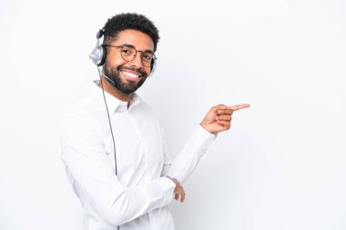 Telemarketer Brazilian man working with a headset isolated on white background pointing finger to the side