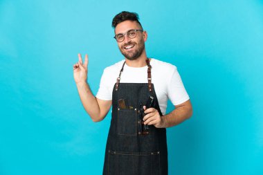 Önlüklü berber gülümsüyor ve zafer işareti gösteriyor.