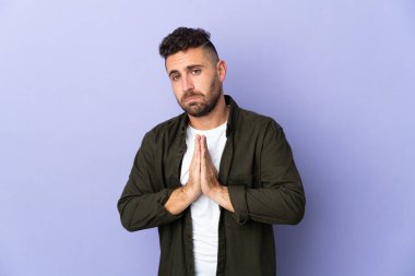Caucasian man isolated on purple background keeps palm together. Person asks for something