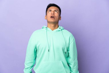 Genç Ekvadorlu adam mor arka planda izole edilmiş yukarı bakıyor ve şaşırmış bir ifadeyle