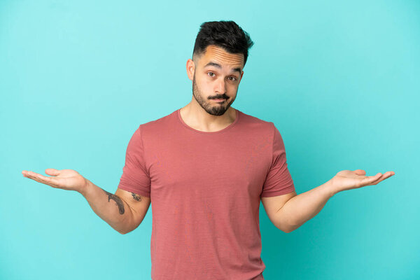 Young caucasian man isolated on blue background having doubts while raising hands
