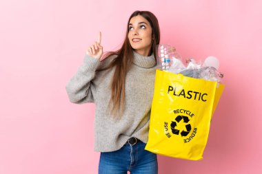 Pembe arka planda izole edilmiş plastik şişelerle dolu bir çanta taşıyan beyaz bir kadın harika bir fikre işaret ediyor.