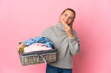 Pembe arka planda izole edilmiş çamaşır sepeti tutan genç bir kadın gülümserken yukarı bakıyor.