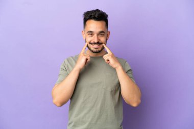 Morarmış arka planda izole edilmiş genç beyaz adam mutlu ve hoş bir ifadeyle gülümsüyor.