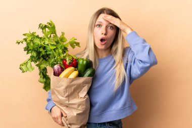 Bir çanta dolusu sebzeyi yalıtılmış arka planda tutan sarışın bir kadın.