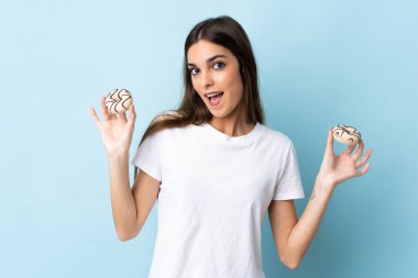 Mavi arka planda izole edilmiş beyaz bir kadın elinde mutlu bir ifadeyle donut tutuyor.