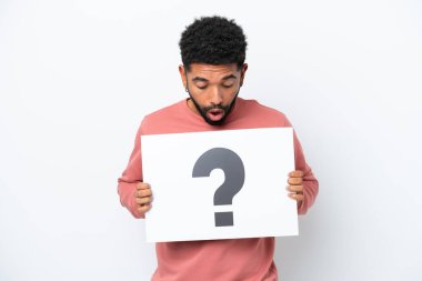 Beyaz arka planda izole edilmiş genç Brezilyalı bir adam soru işareti sembollü bir levha tutuyor.