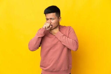 Genç Ekvadorlu adam sarı arka planda çok öksürüyor.