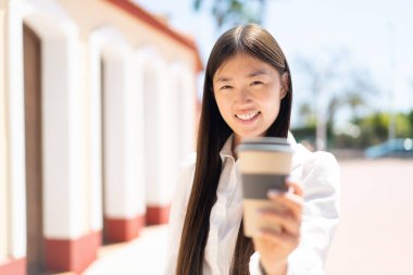 Dışarıdaki güzel Çinli kadın elinde neşeli bir ifadeyle kahveyi tutuyor.