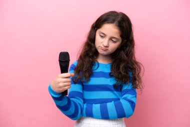 Pembe arka planda üzgün bir ifadeyle izole edilmiş bir mikrofonu kaldıran küçük şarkıcı kız.