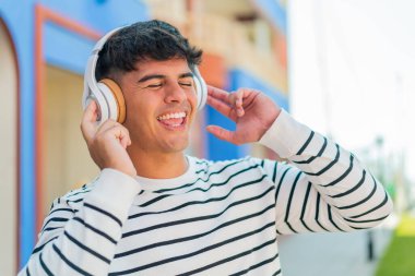 Genç İspanyol adam açık havada müzik dinliyor ve şarkı söylüyor.