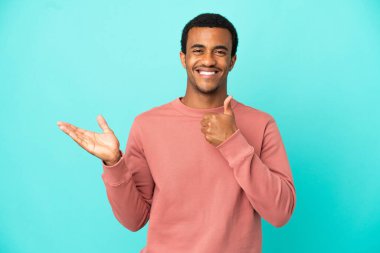 İzole edilmiş mavi arka planda Afro-Amerikalı yakışıklı bir adam. Avucunun içinde hayali bir şey tutuyor. Bir ilan vermek için.