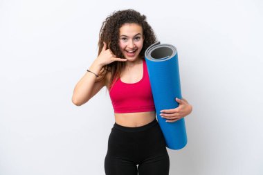 Genç Arap spor kadını yoga derslerine giderken beyaz arka planda izole edilmiş bir minder tutarak telefon jesti yapıyor. Bana geri dönüş işareti ver.