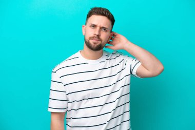 Kafkasyalı genç adam mavi arka planda izole edilmiş. Şüpheleri var.