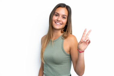 Beyaz arka planda izole edilmiş genç beyaz kadın gülümsüyor ve zafer işareti gösteriyor.