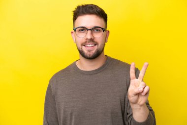 Sarı arka planda gözlüklü, tamam işareti olan genç beyaz bir adam.