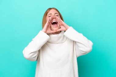Genç kızıl saçlı kadın mavi arka planda izole edilmiş bağırıyor ve bir şeyler söylüyor.