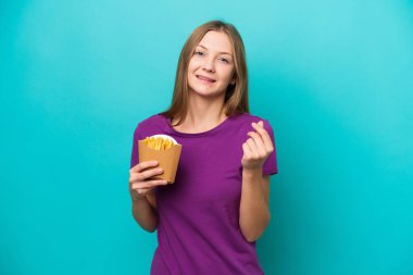 Mavi arka planda izole edilmiş patates kızartması yakalayan genç Rus kadın para hareketi yapıyor.