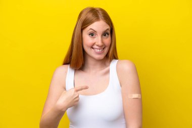 Sarı arka planda yara bandı takan genç, kızıl saçlı bir kadın.