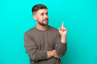 Mavi arka planda izole edilmiş genç beyaz adam harika bir fikre işaret ediyor.