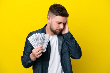 Kafkasyalı genç bir adam çok para alıyor sarı arka planda izole edilmiş ve başı ağrıyan.