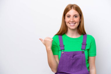 Beyaz arka planda izole edilmiş genç kızıl saçlı kadın bir ürünü sunmak için kenarı işaret ediyor.