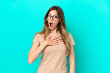 Mavi arka planda izole edilmiş genç beyaz kadın sağa bakarken şaşırdı ve şok oldu.