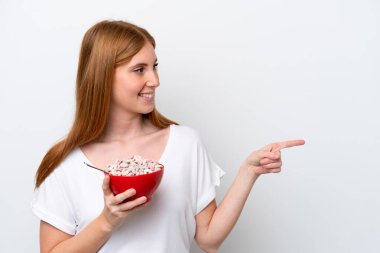 Genç kızıl saçlı kadın beyaz arka planda izole edilmiş bir kase mısır gevreği tutuyor.