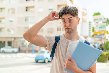 Açık havada genç yakışıklı bir öğrencinin kuşkuları var ve kafası karışmış bir yüz ifadesi var.