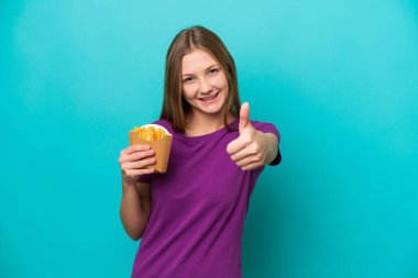 Patates kızartması yakalayan genç Rus kadın mavi arka planda izole edildi. Başparmakları havada çünkü iyi bir şey oldu.