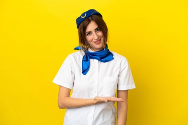 Uçak hostesi kadın sarı arka planda izole edilmiş bir şekilde gülümserken bir fikir sunuyor.