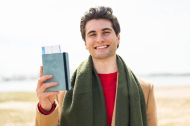 Dışarıda elinde pasaport tutan yakışıklı genç adam çok gülümsüyor.