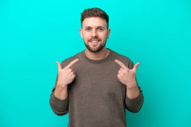 Mavi arka planda izole edilmiş genç beyaz adam mutlu ve hoş bir ifadeyle gülümsüyor.