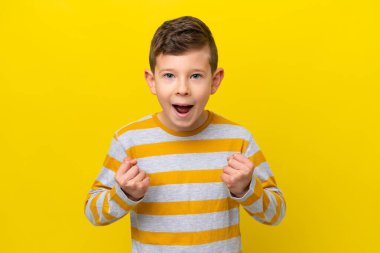 Sarı arka planda izole edilmiş küçük beyaz çocuk galibiyeti kutluyor.