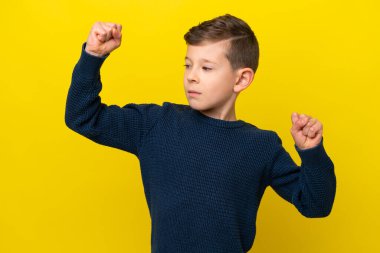 Sarı arka planda izole edilmiş küçük beyaz çocuk güçlü bir jest yapıyor.