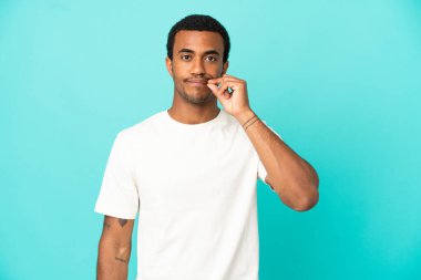 İzole edilmiş mavi arka plandaki Afro-Amerikalı yakışıklı adam sessizlik işareti gösteriyor.