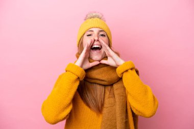 Kışlık ceket giyen genç kızıl saçlı kadın pembe arka planda izole edilmiş bağırıyor ve bir şey duyuruyor.