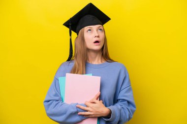 Sarı arka planda izole edilmiş genç bir Rus öğrenci yukarı bakıyor ve şaşırmış bir ifadeyle