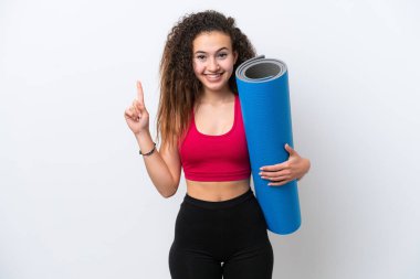 Genç Arap spor kadını yoga derslerine giderken beyaz arka planda izole edilmiş bir minder tutuyor ve harika bir fikre işaret ediyor.