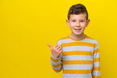 Sarı arka planda izole edilmiş küçük beyaz çocuk bir ürün sunmak için kenarı işaret ediyor.