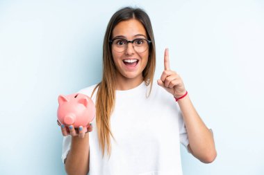 Elinde kumbarası olan beyaz bir kadın mavi arka planda izole edilmiş bir şekilde harika bir fikre işaret ediyor.